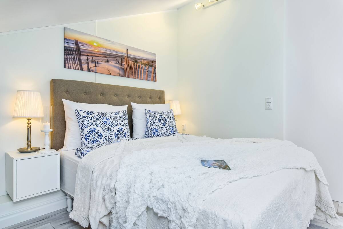 A neatly arranged bedroom with a large bed, white bedding, and a sunset painting above it.