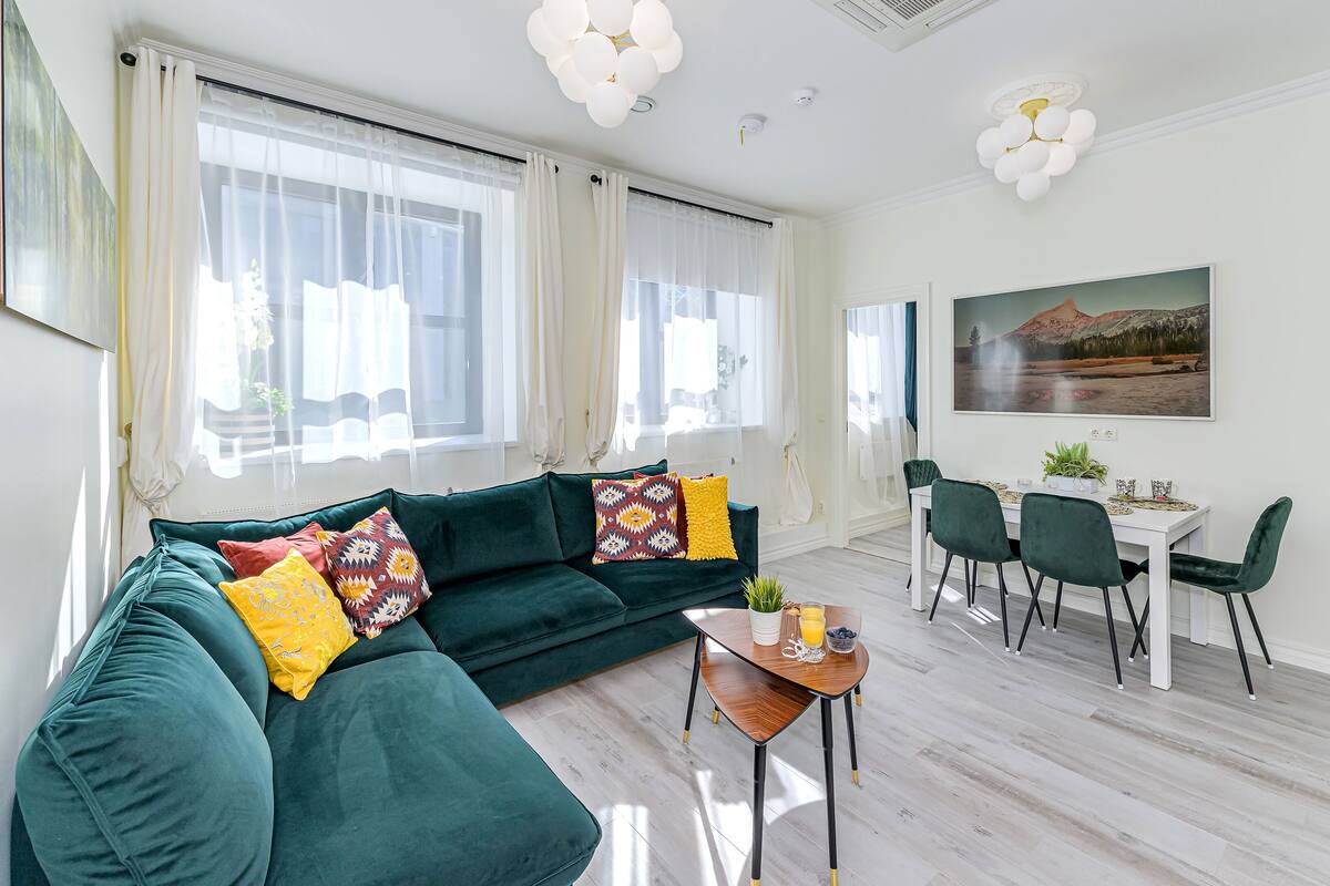 A modern living room with a green sofa, a wooden coffee table, and a dining area with a white table and green chairs.