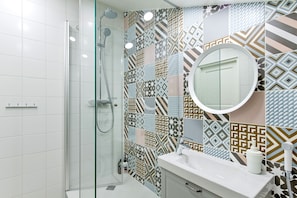A modern bathroom with a glass-enclosed shower, a white sink, and a mirror with a round frame. - Harbor Black Pearl Apartments (Tallinn)