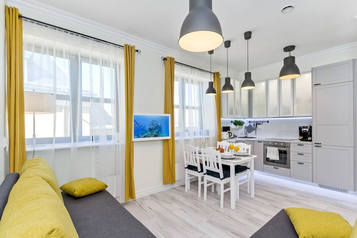 A modern kitchen with white cabinets, a dining table with chairs, and pendant lights.