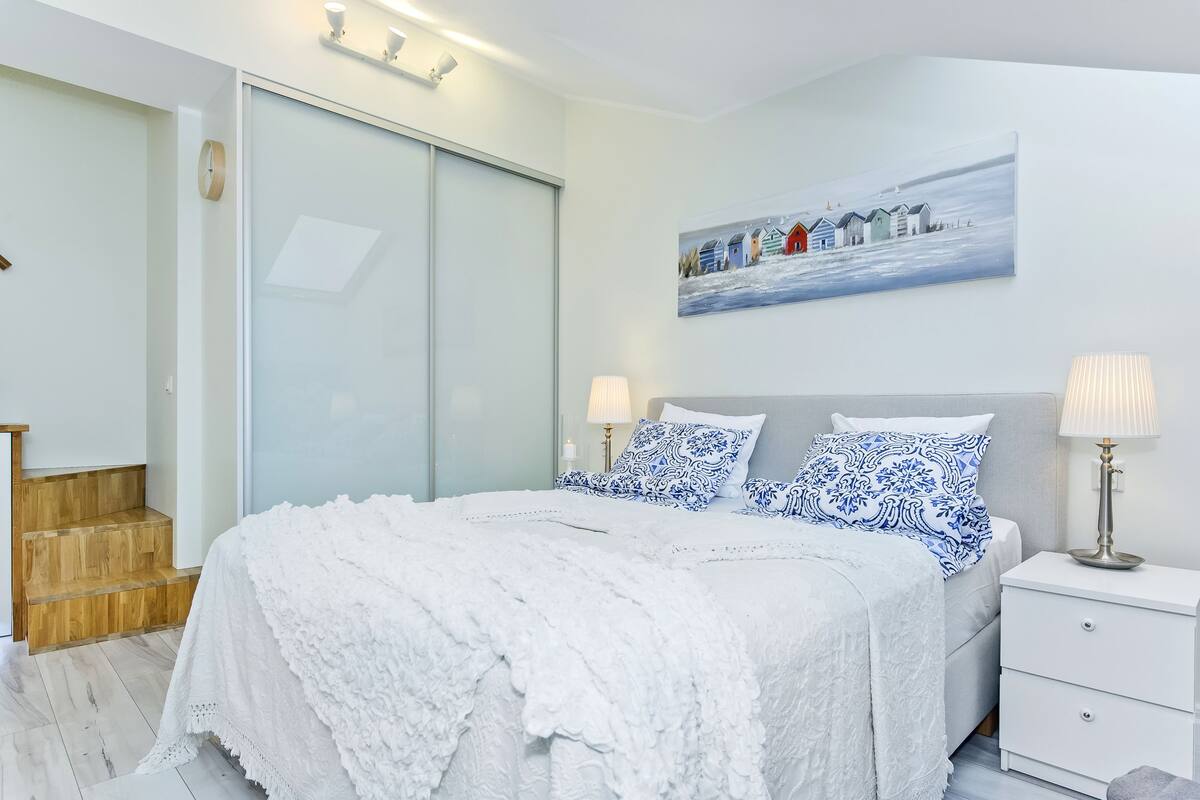 A bedroom with a bed, bedside tables, a nightstand, a painting on the wall, and a sliding door.