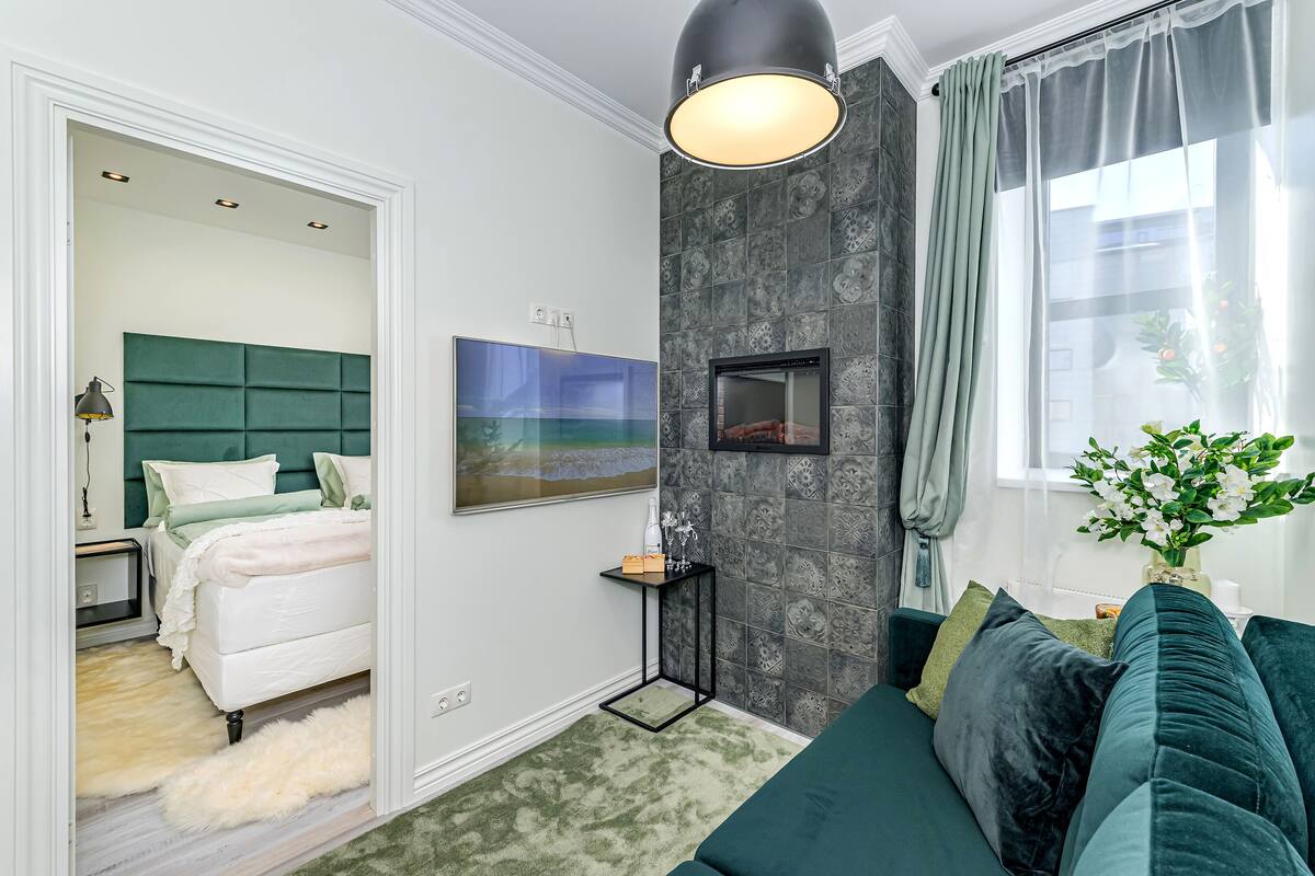 A modern bedroom with a green upholstered headboard, a flat-screen TV, and a bedside table with a lamp.