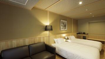 Een hotelkamer met een houten hoofdbord, twee bedden met witte lakens, een zwarte leren bank, een nachtkastje met een lamp en een ingelijst schilderij aan de muur.