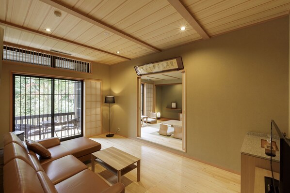 Ein traditionelles japanisches Wohnzimmer mit Tatami-Böden, einem niedrigen Holztisch, einer Couch und einer Schiebetür zu einem Essbereich.