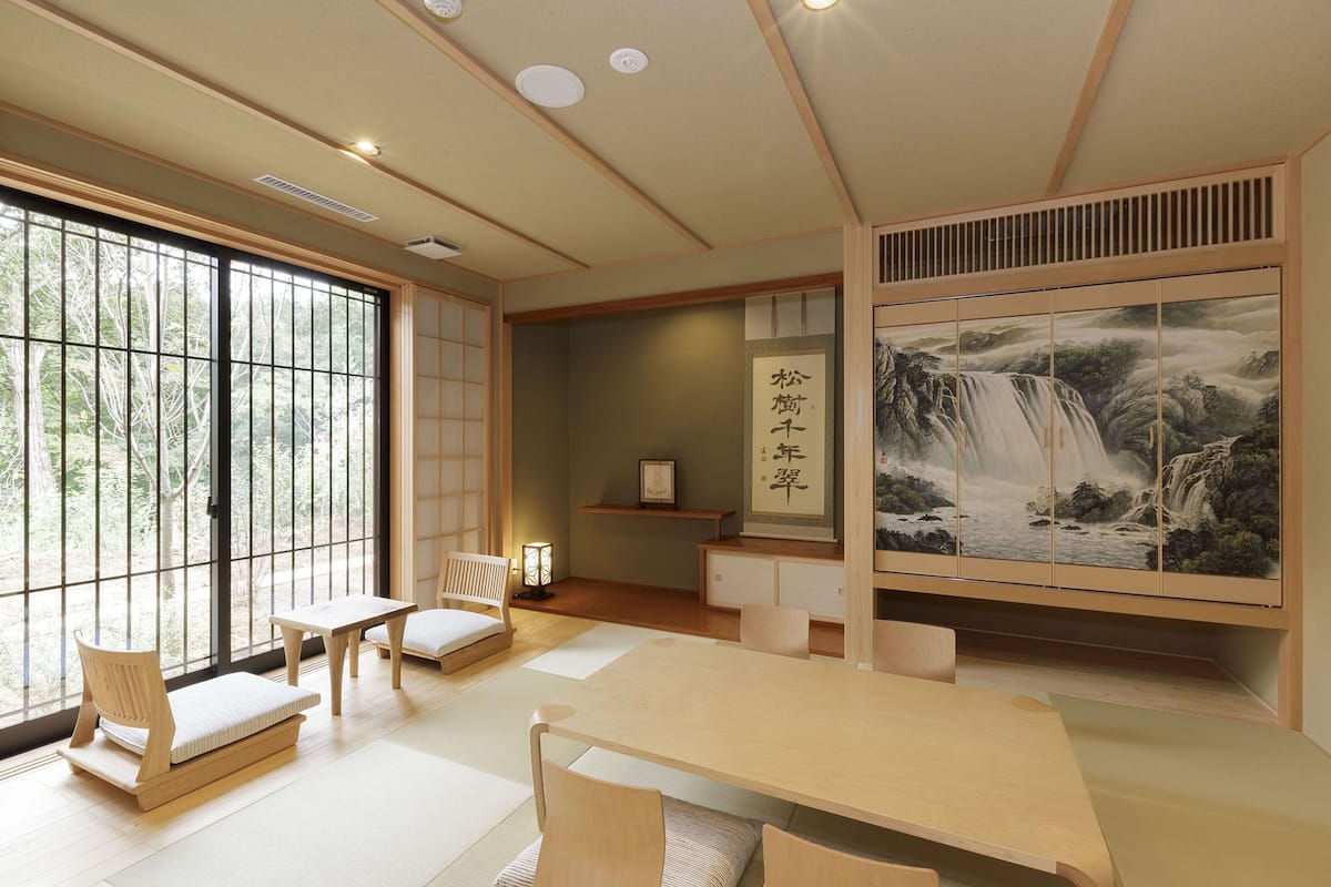 Une pièce de style japonais traditionnel, avec un sol recouvert de tatamis, une table basse et une grande fenêtre donnant sur la forêt.