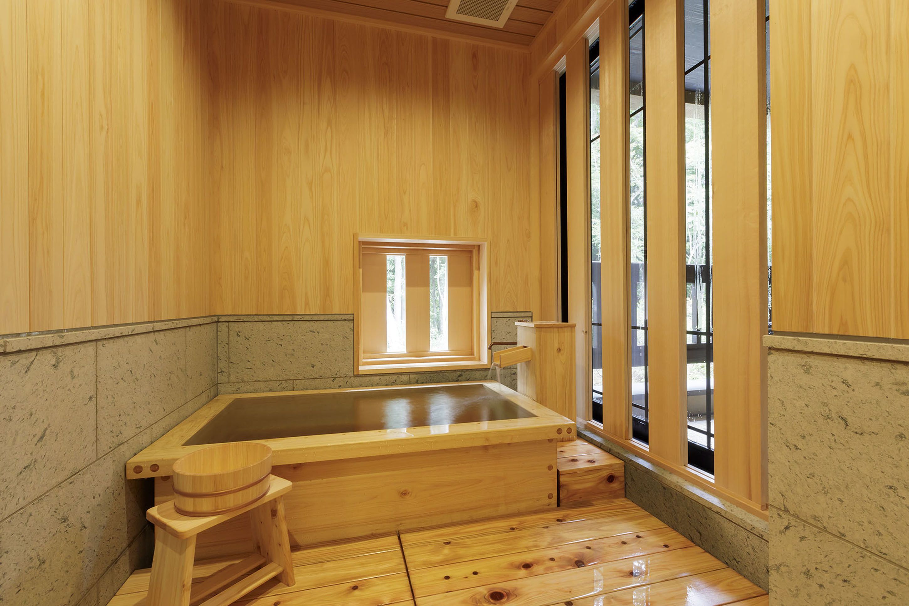 A wooden spa room with a large bathtub, a wooden bench, and a window.