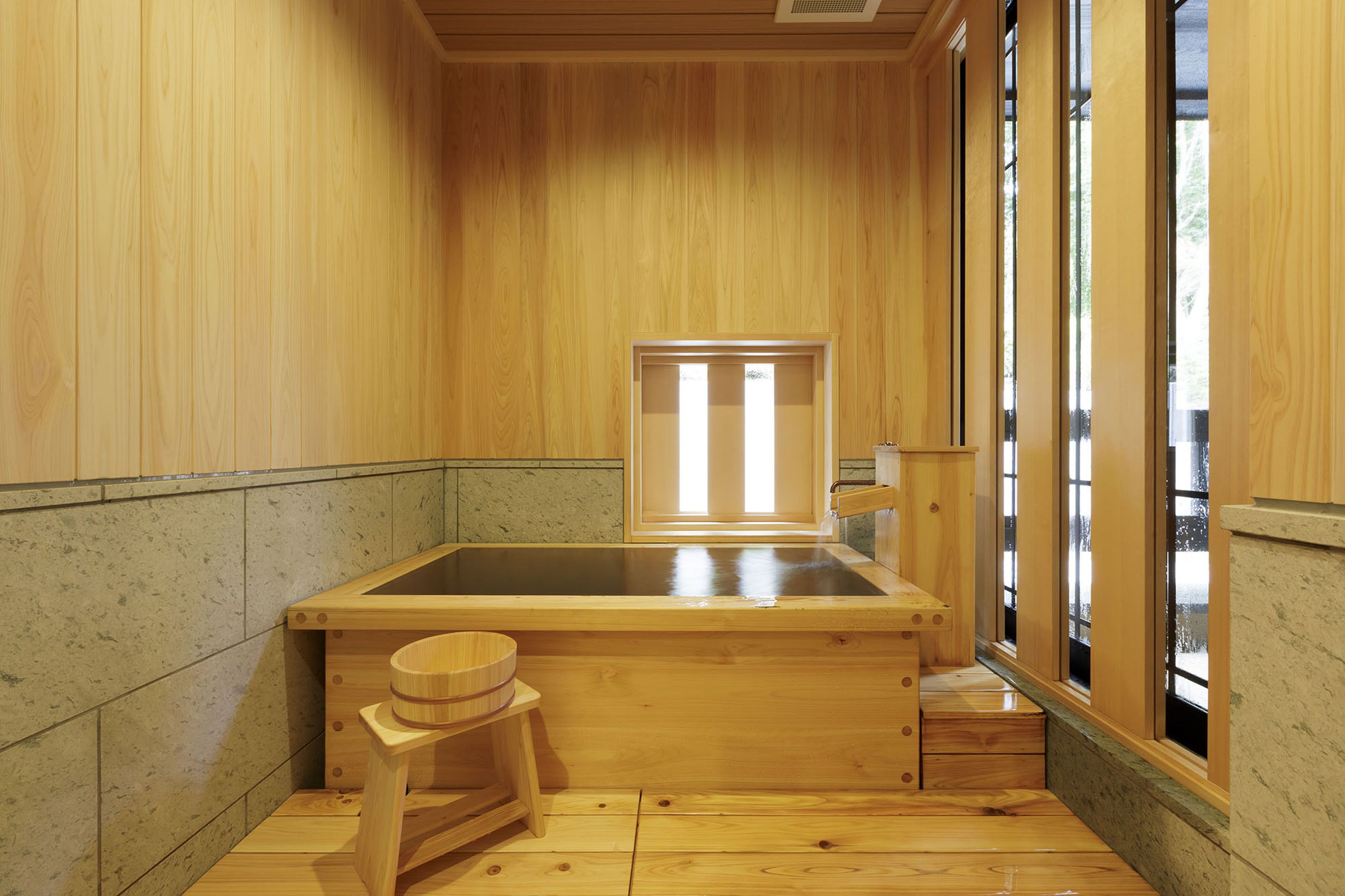 A traditional wooden bath with a sliding door, a wooden stool, and a small wooden shelf.