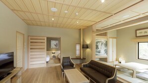 Ein modernes Wohnzimmer mit Sofa, Sesseln, Fernseher und Bett.