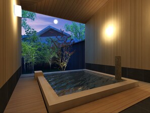 Ein modernes Spa mit Holzinneneinrichtung, einer Whirlwanne und Blick auf ein traditionelles Gebäude sowie Bäume.