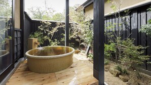 Eine Holzterrasse mit Whirlpool, umgeben von einem Garten mit verschiedenen Pflanzen und einem Holzzaun.