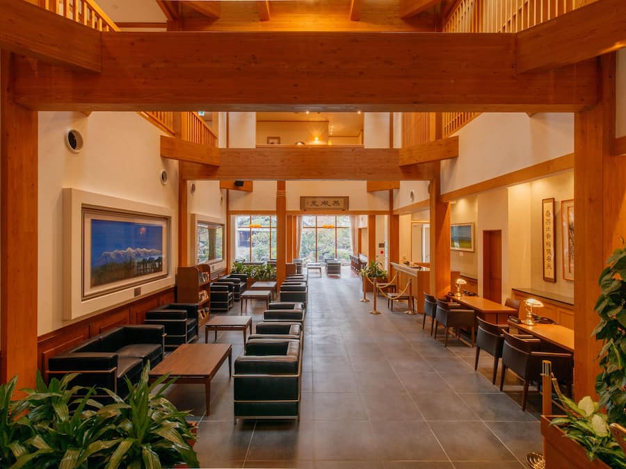 A spacious hotel lobby with wooden beams, seating areas, and large windows offering views of the outdoors.