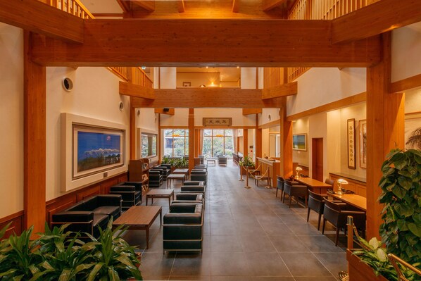 A spacious hotel lobby with wooden beams, seating areas, and large windows offering views of the outdoors.