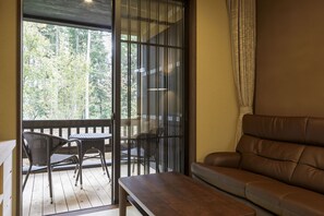 Ein Balkon mit Korbmöbeln, einem Ledersofa und Blick auf Bäume.