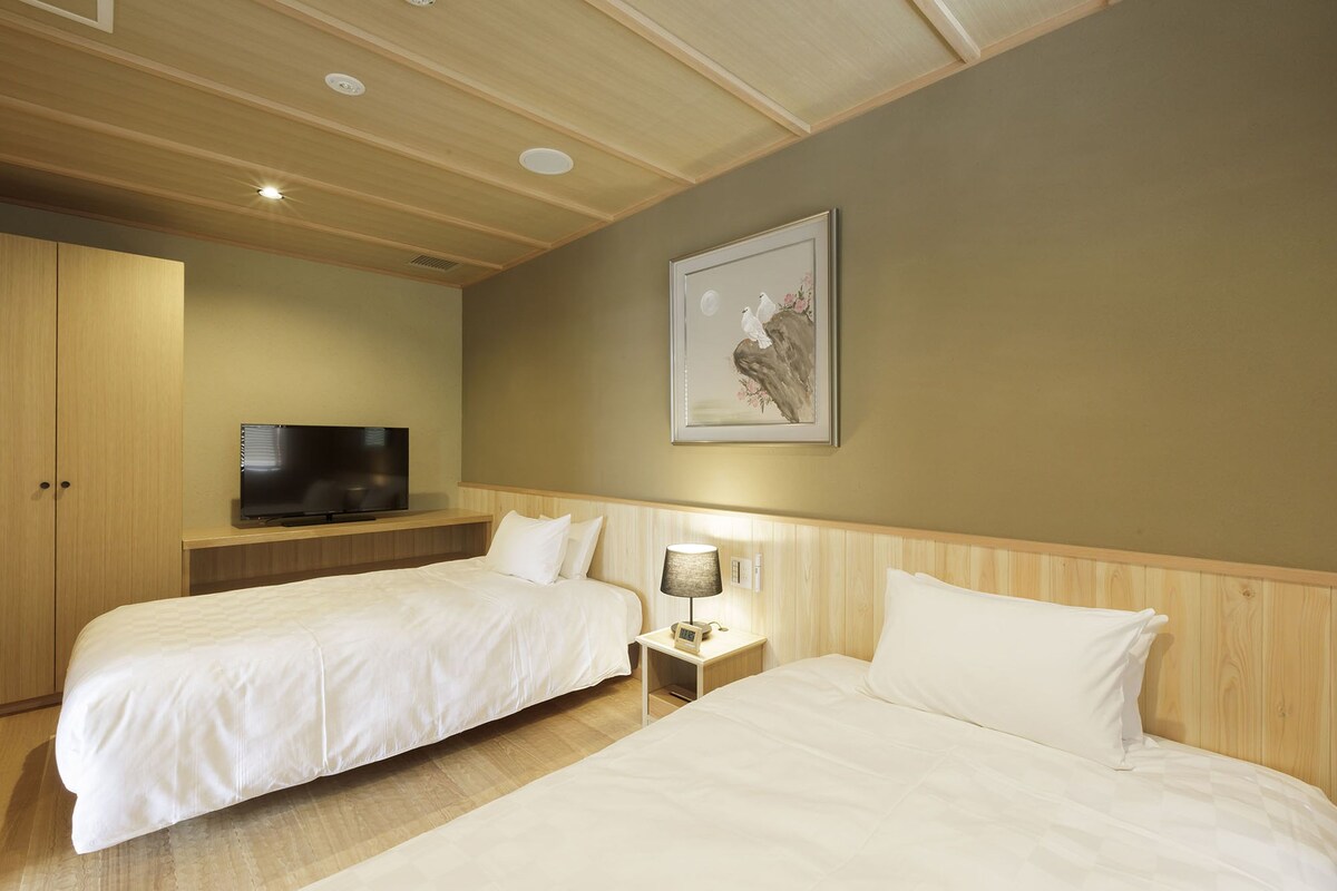 A hotel room with two beds, a television, a painting, and a nightstand with a lamp.