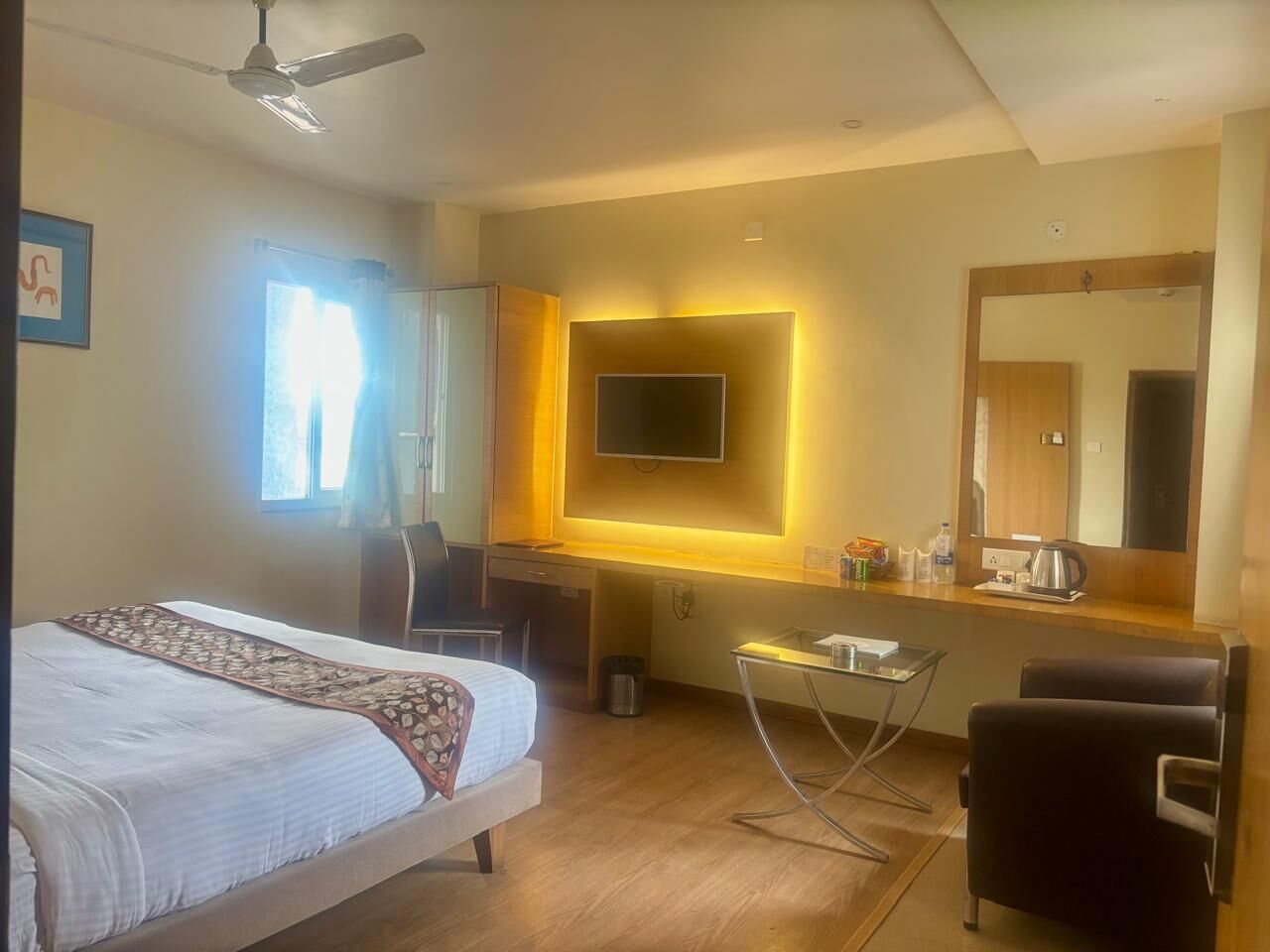 Een hotelkamer met een bed, bureau, stoel, televisie en een grote spiegel.