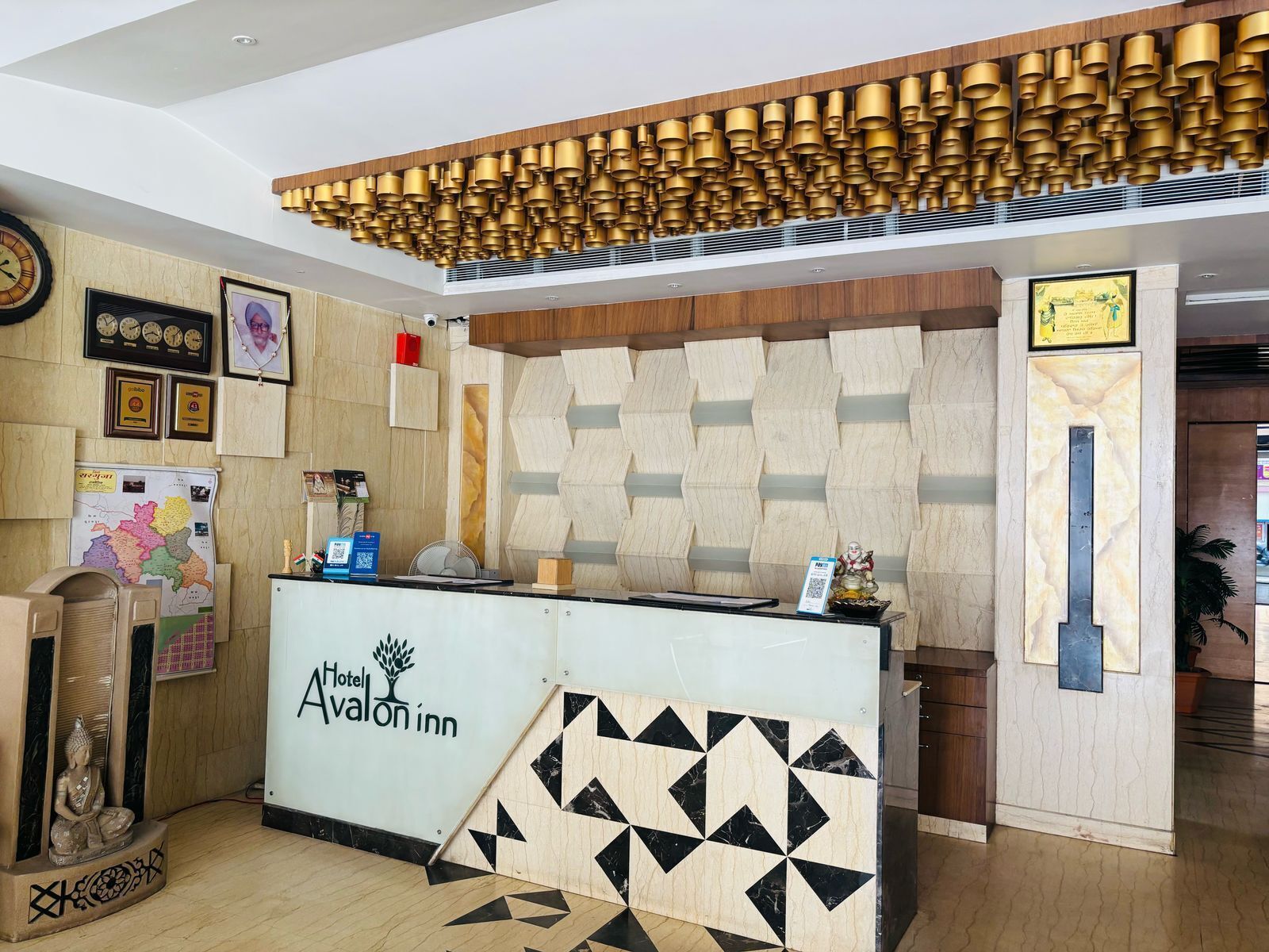 A hotel reception desk with a geometric patterned counter, a Buddha statue, and a wall-mounted clock.