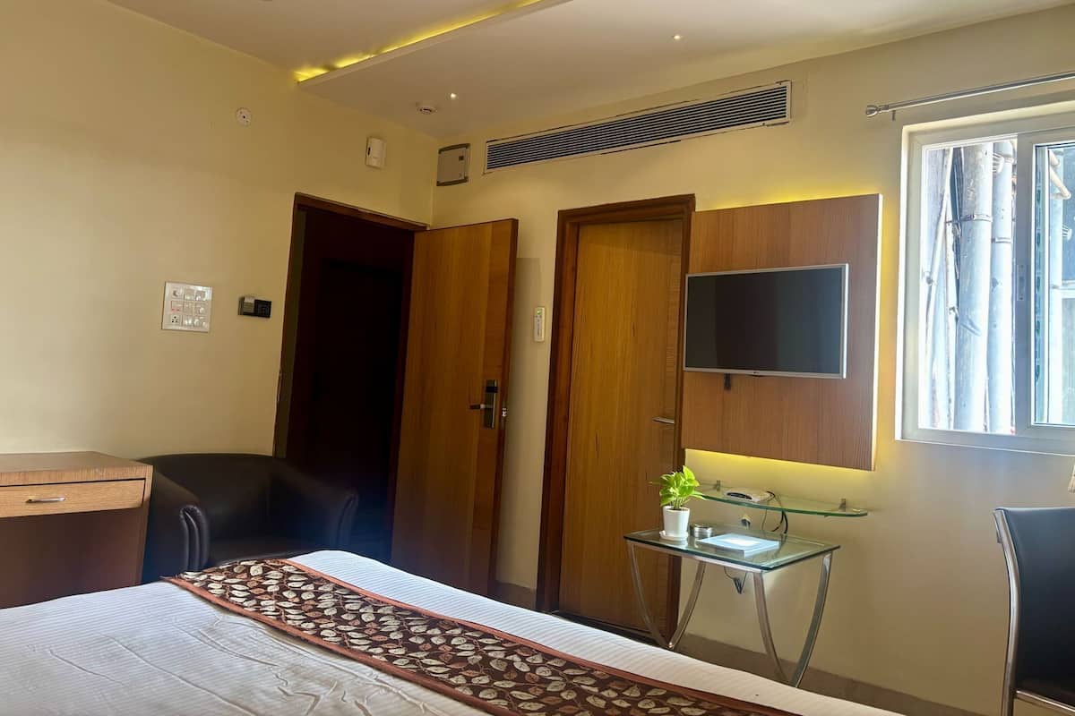 A hotel room with a bed, a desk, a chair, a TV mounted on the wall, and a window with a view of trees.