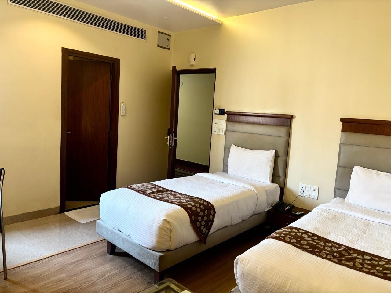 Une chambre d’hôtel avec deux lits, une porte en bois, un miroir et une table de chevet.
