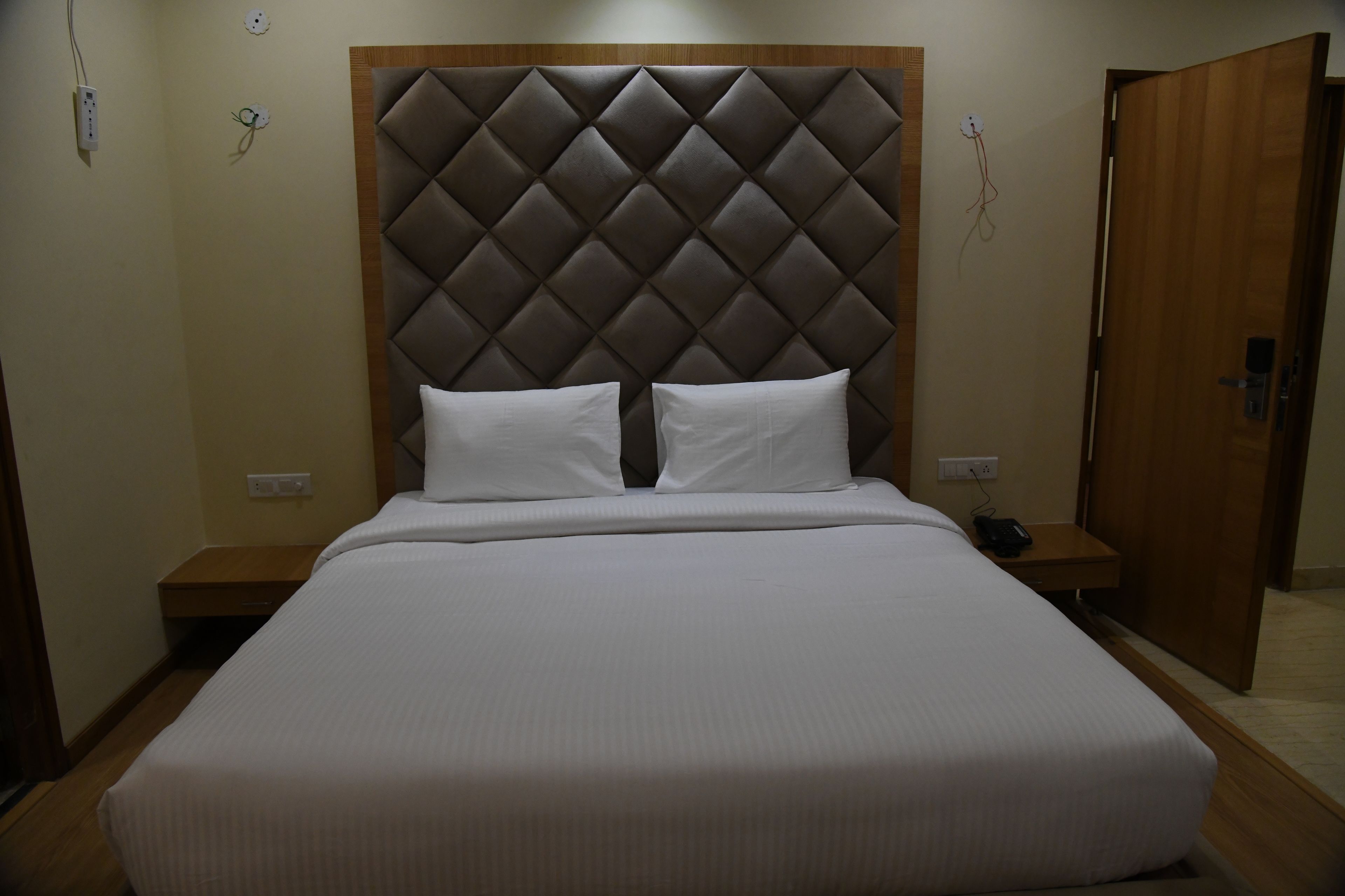 A neatly made bed with a tufted headboard, two bedside tables, and a wooden door.