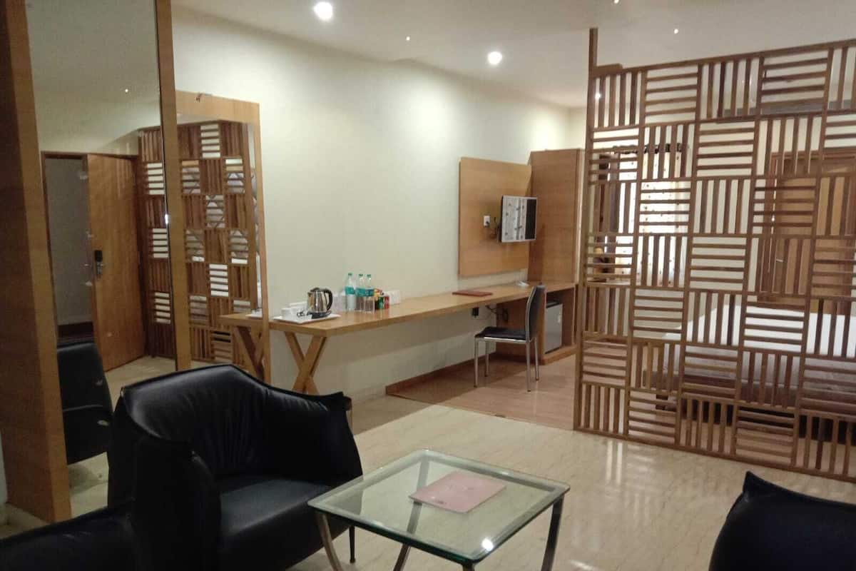 A modern hotel room with a glass coffee table, black leather sofa, wooden partition, and a desk with a computer and water bottles.