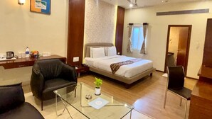 Habitación de hotel con cama, una mesita de vidrio, un sillón de cuero negro, un escritorio con lámpara y una planta pequeña.