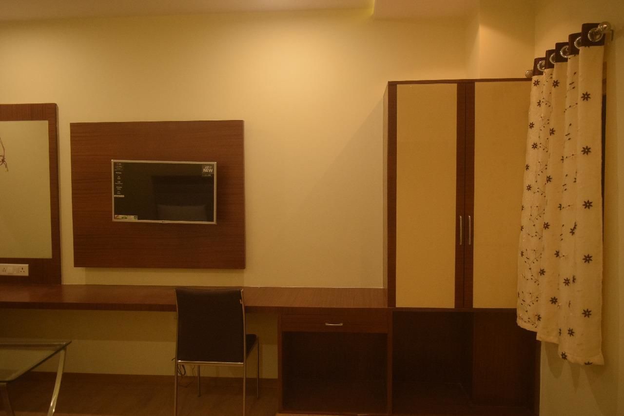 A bedroom with a bed, a desk, a chair, a wardrobe, and a television mounted on the wall.