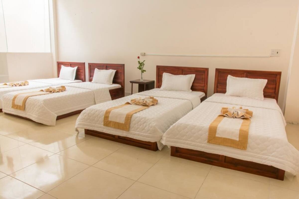 A hotel room with three beds, each with white bedding and a wooden headboard.