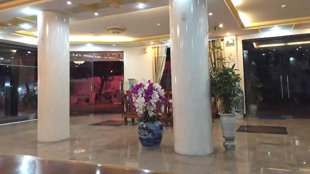 A lobby with a polished marble floor, large white columns, and a blue vase with purple flowers.