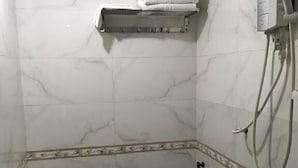 A small, tiled bathroom with a toilet, a shower, and a towel rack.