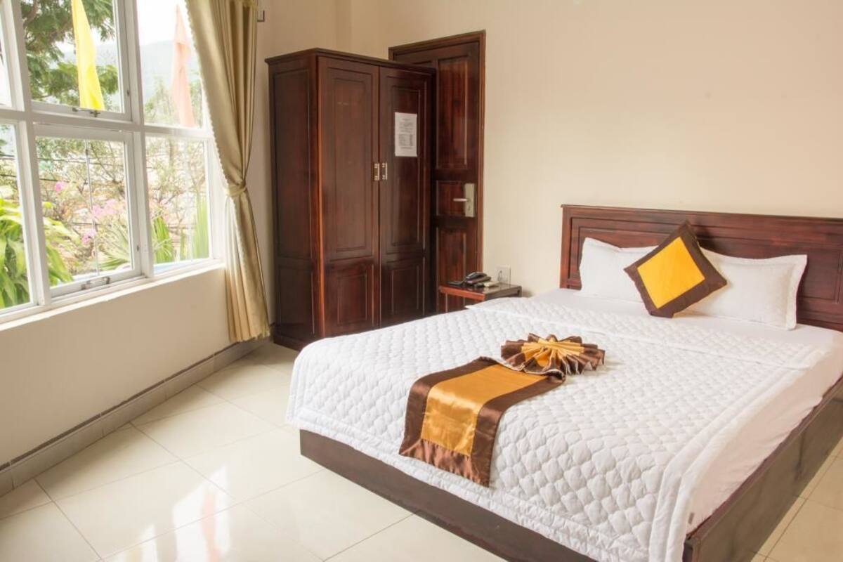 A hotel room with a large bed, wooden wardrobe, and a window with curtains.