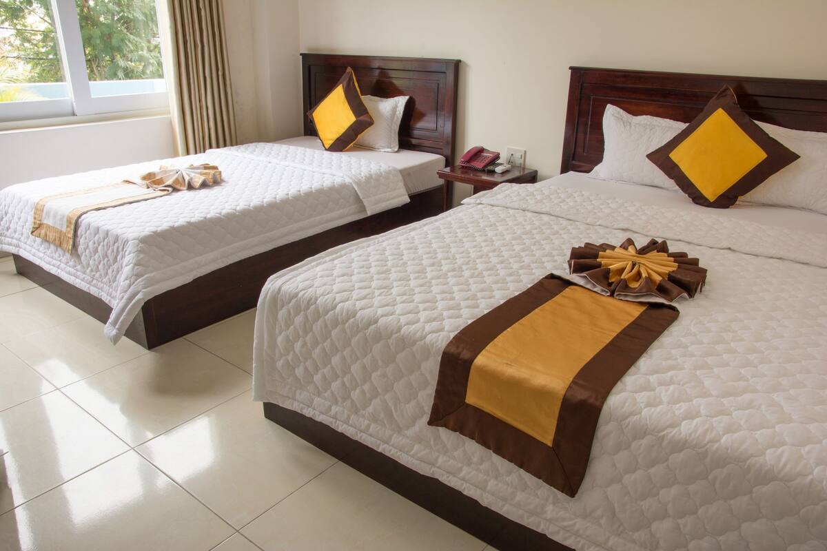 Two queen-sized beds with white quilts and brown accents, a wooden headboard, and a bedside table with a telephone.