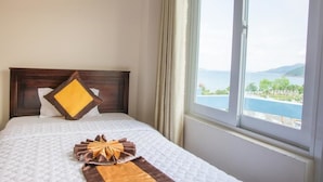A hotel room with a bed, a view of a body of water, and a window with curtains.