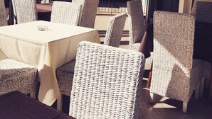 A restaurant with wicker chairs and tables, a glass railing, and a view of the street. - Hotel Riva (Rimini)
