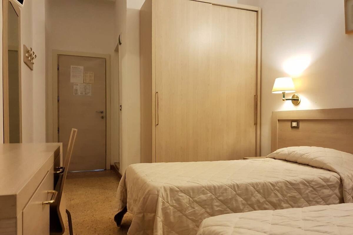 A hotel room with two beds, a desk, and a wardrobe.