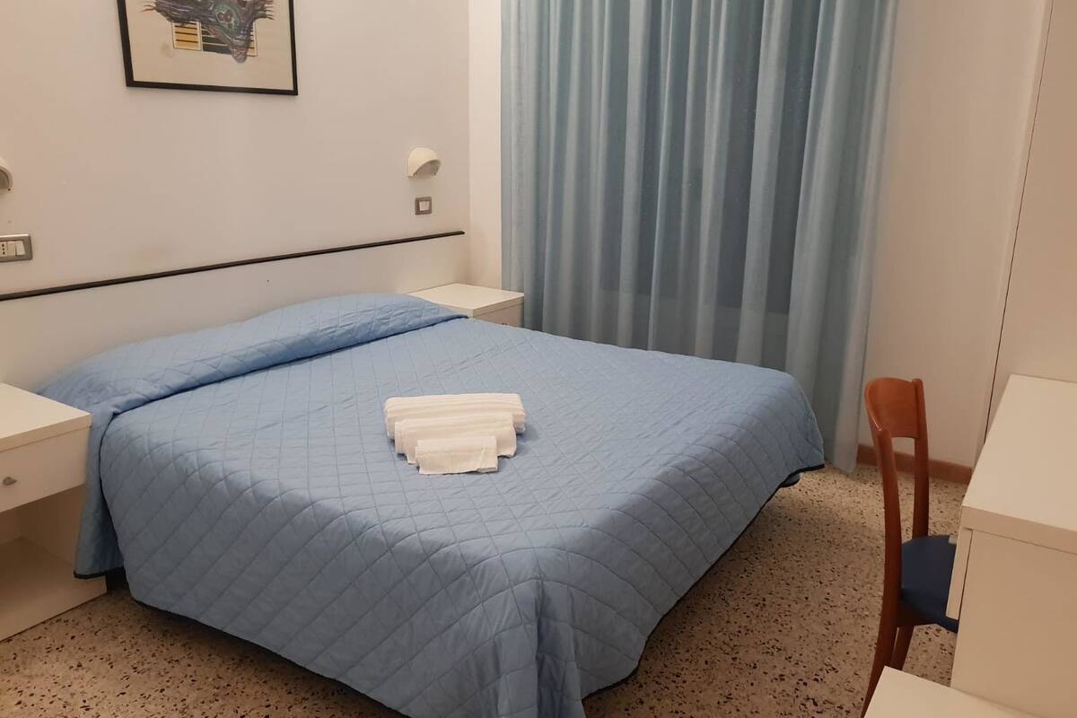 A hotel room with a bed, a nightstand, a chair, and a desk.
