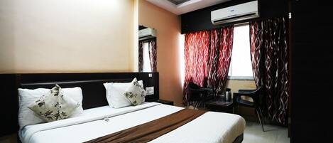 Hotelkamer met een bed, een bureau, een stoel, een airconditioning en een raam met gordijnen.