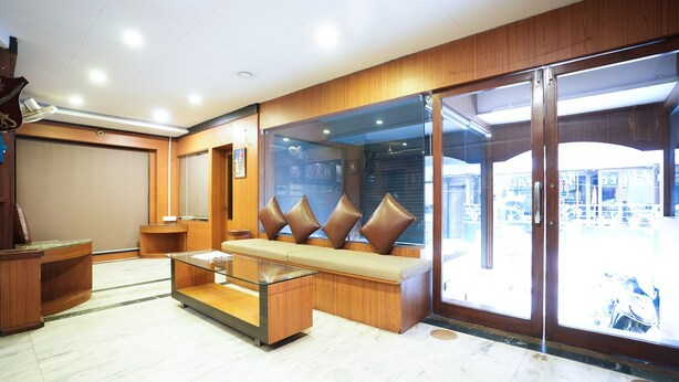 A modern lobby with a seating area, a reception desk, and a glass door leading outside. - HOTEL MADURAI (Udaipur)