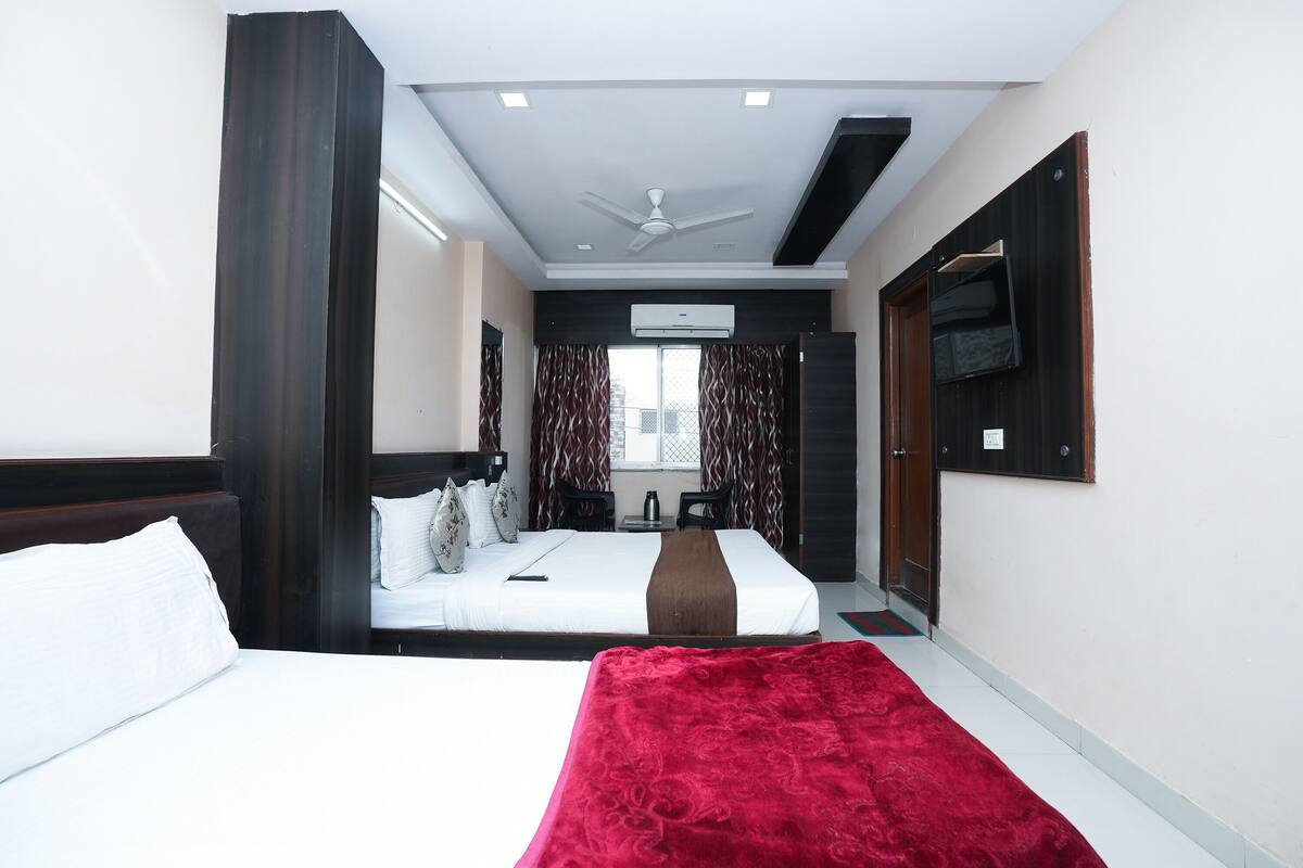 Habitación de hotel con cama, una manta roja, ventilador de techo y televisor montado en la pared.