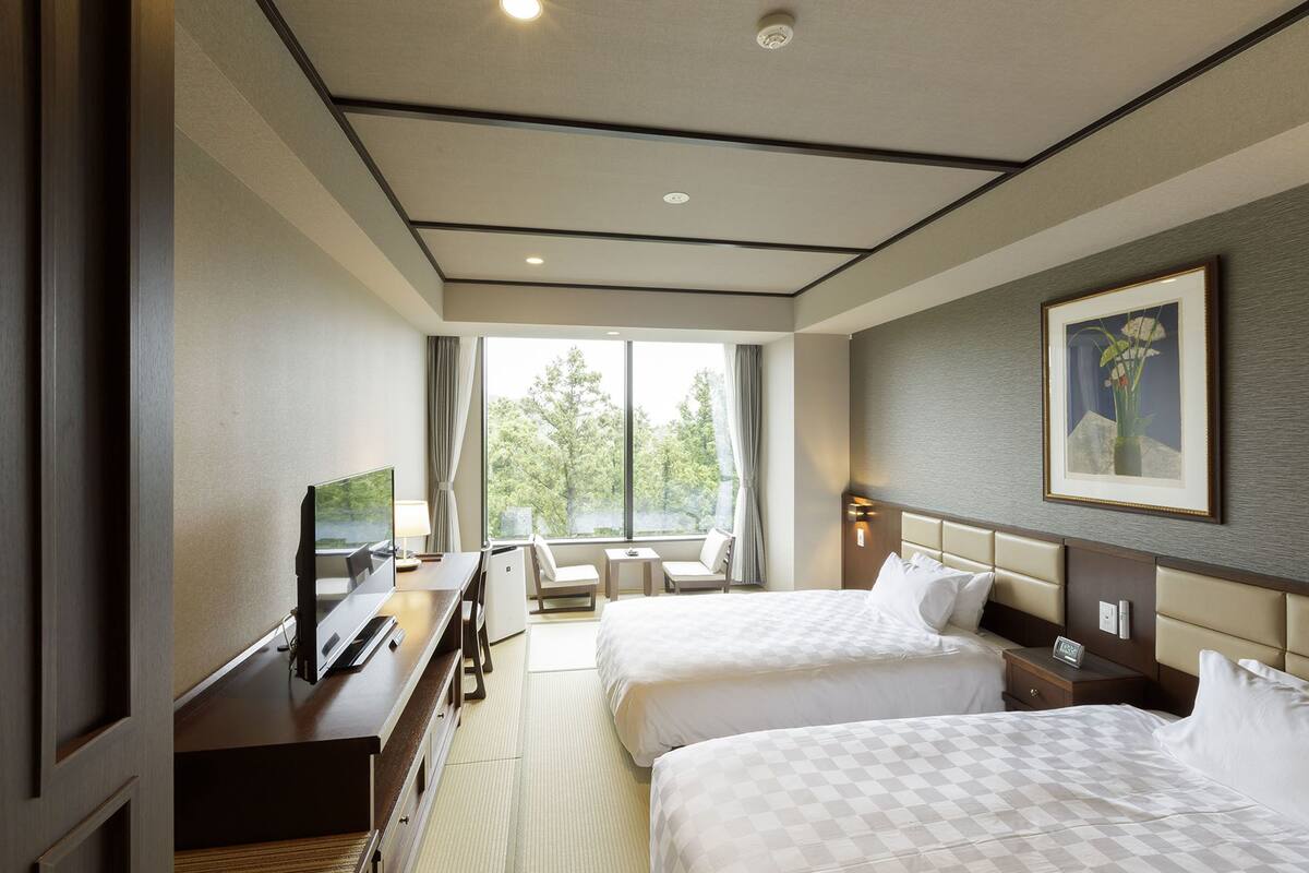 Habitación de hotel con dos camas, un escritorio con televisor, una mesita pequeña y una silla.