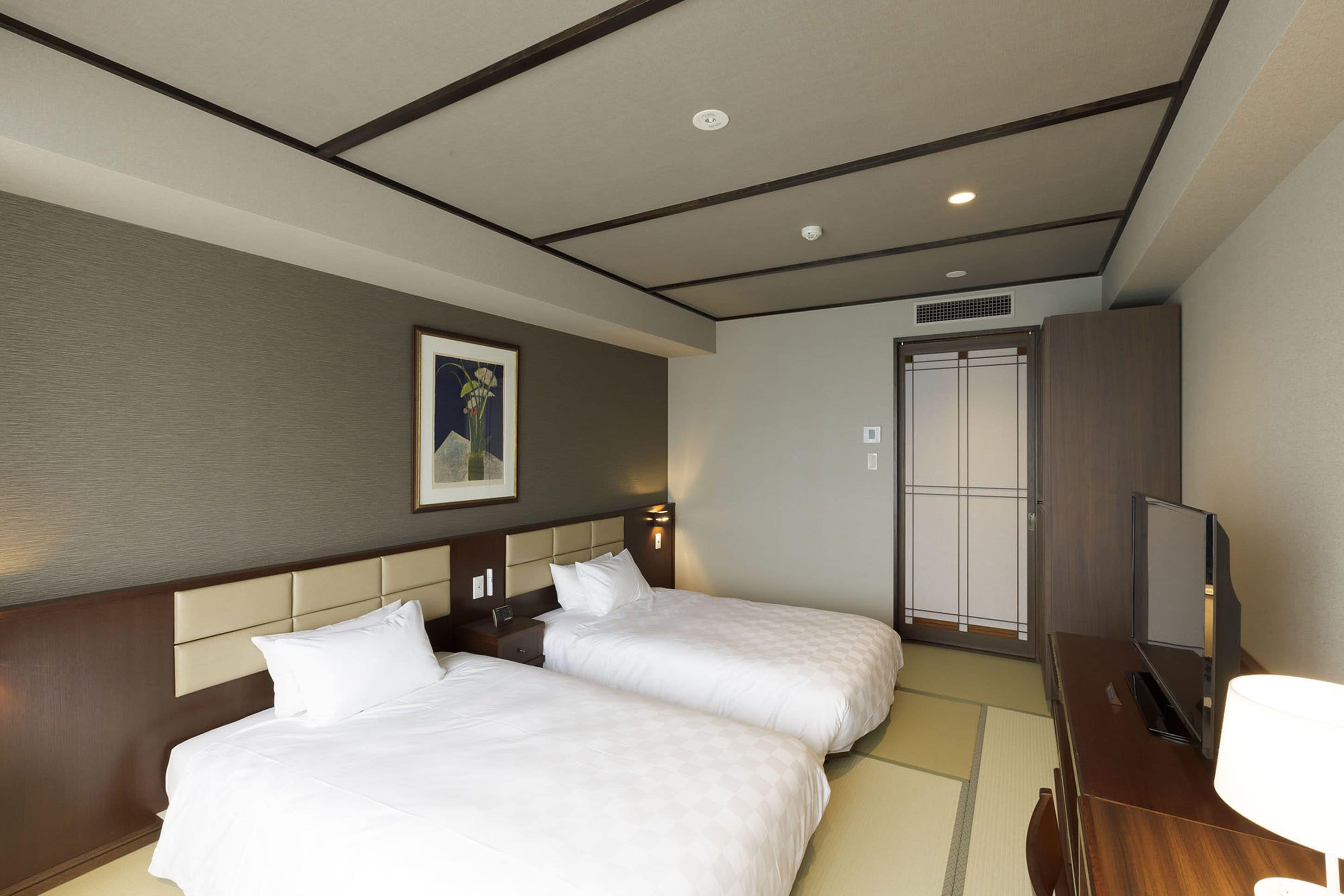 A hotel room with two beds, a television, a painting on the wall, and a sliding door.