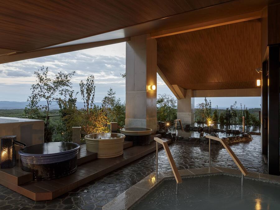 A spa area with hot tubs and a stone pool, surrounded by wooden deck and large windows overlooking a natural landscape.