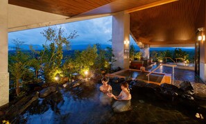 Un site de sources chaudes offrant une vue sur les montagnes, avec une terrasse en bois et une architecture en pierre.