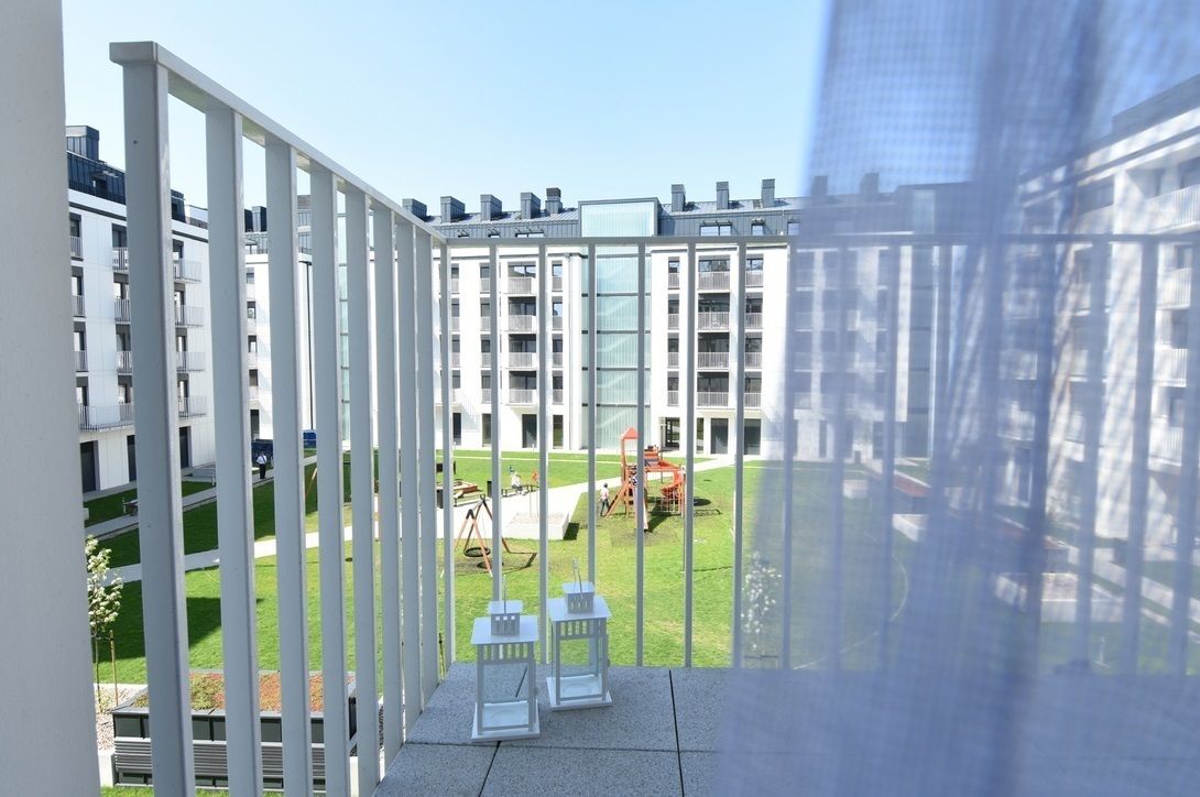 Een modern appartementencomplex met balkons, een gazon en buitentafels.