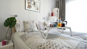Ein ordentlich eingerichtetes Hotelzimmer mit einem Bett, einem Nachttisch mit Kaffeemaschine, einer großen Pflanze und einem gerahmten Bild an der Wand.