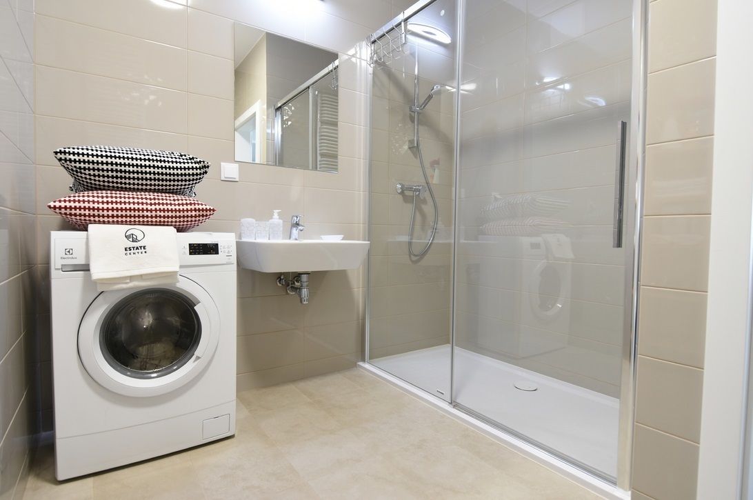 Un bagno moderno con doccia vetro, lavatrice e lavandino.