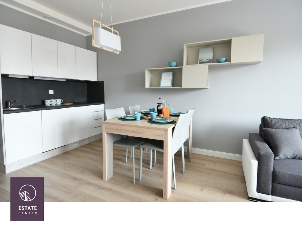 A modern kitchen with white cabinets, a dining table with chairs, and a grey sofa.