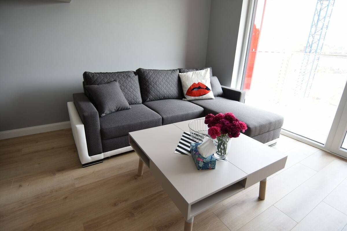 Een moderne woonkamer met een grijze bank, een witte salontafel en een vaas met bloemen.
