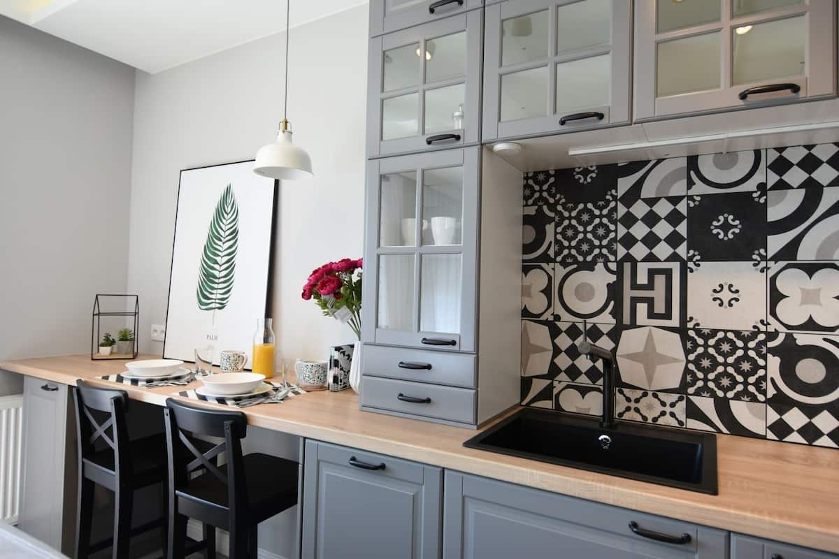 Een moderne keuken met grijze kastjes, een zwarte spoelbak en een decoratieve achterwand.