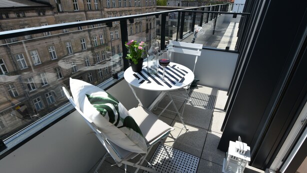 Ein Balkon mit einem weißen Tisch, einem weißen Stuhl, einem Blumentopf und einem Weinglas.