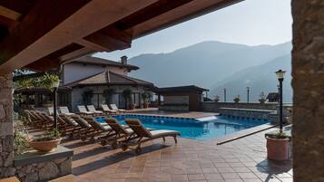 Un espace piscine avec des chaises longues, un mur en pierre et une vue sur les montagnes.